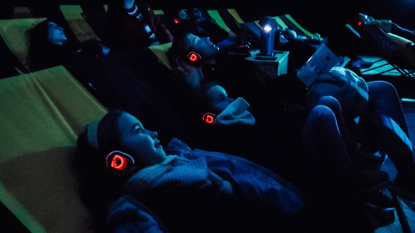 Visitors relax in deck chairs wearing headsets during an immersive planetarium experience.