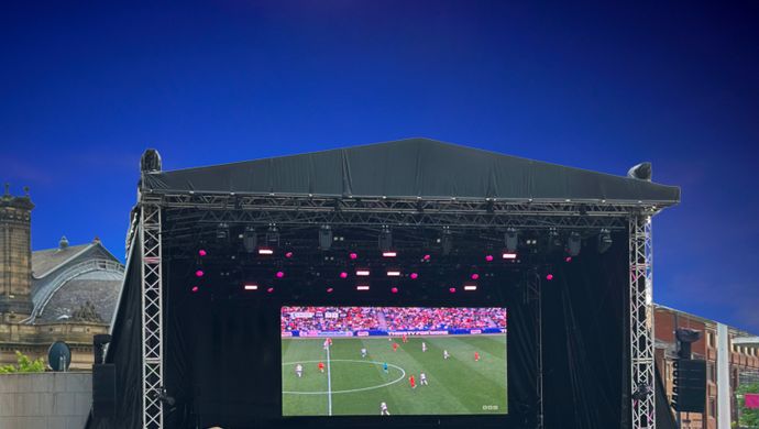 Football match shown on a screen set up on stage in front of thousands of fans