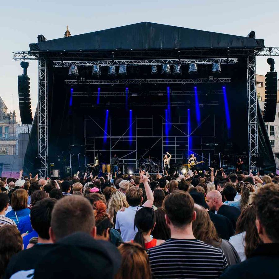 Outdoor concert crowd facing a large stage with blue lighting and performers at the centre.