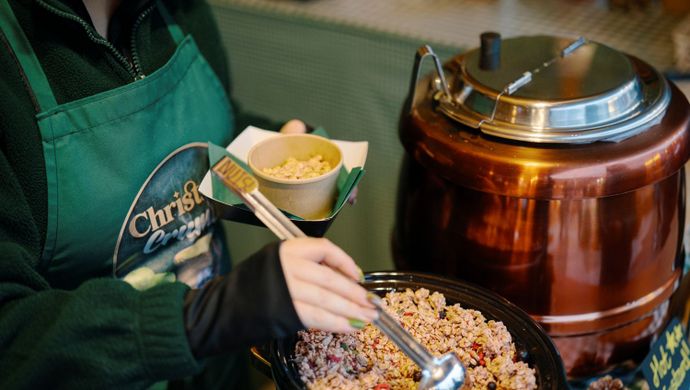 Vendor serving a bowl of crumble from a market stall.