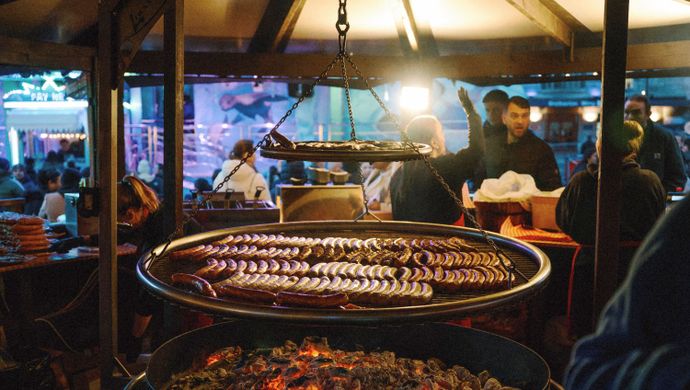 Large circular grill cooking bratwurst over an open fire.