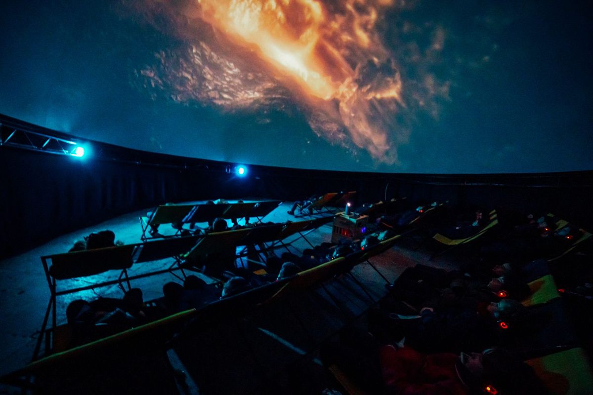 Visitors watch an immersive space projection inside a 360° planetarium dome.