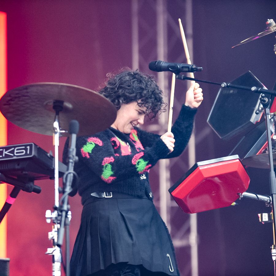 Georgia playing electronic drums on stage at Millennium Square, surrounded by percussion equipment with warm red lighting in the background.