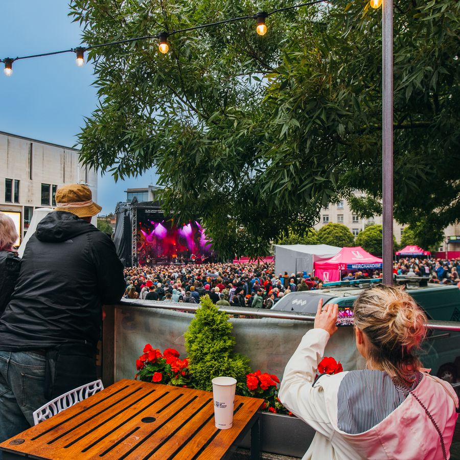 3 people facing back looking and taking pictures at the gig happening on the square.