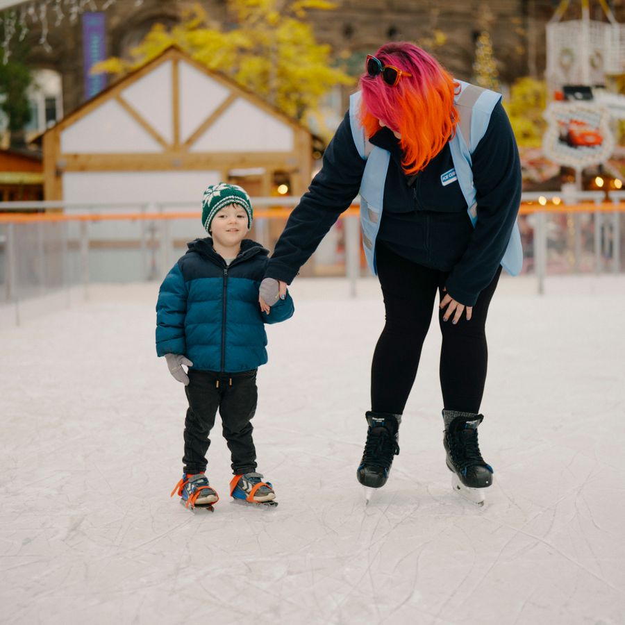 Child holding hands with a skating coach during a beginner ice skating lesson