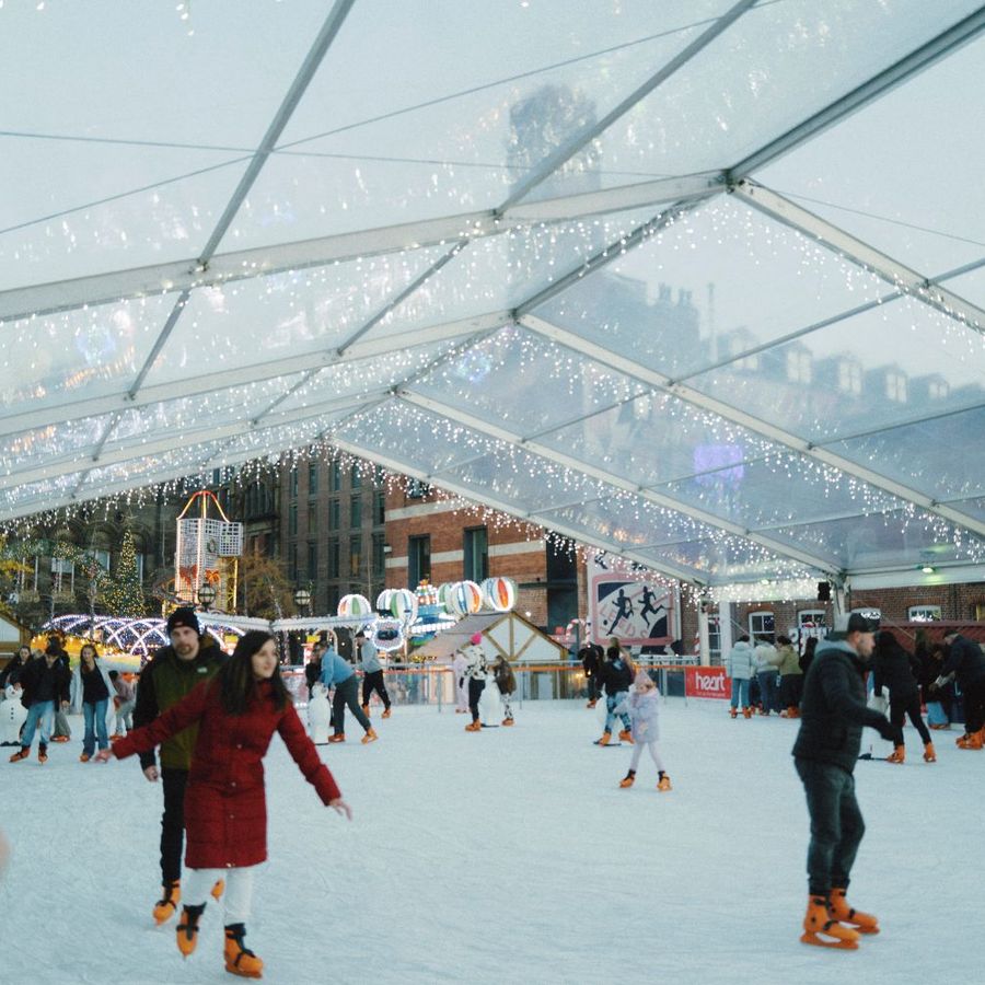 People ice skating on the covered outdoor rink decorated with festive lights.