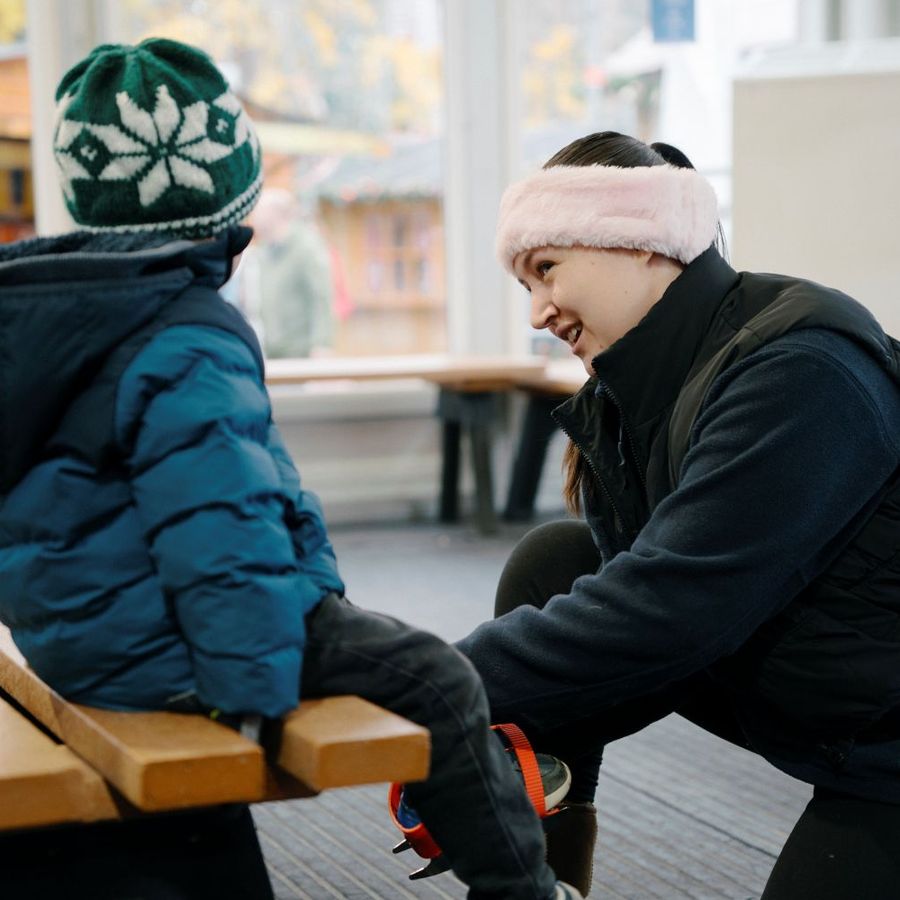 Member of staff helping a child put on ice skates beside the rink at Ice Cube at Christmas.
