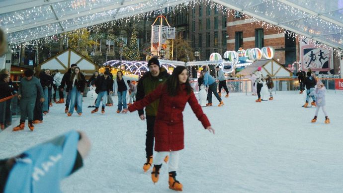 People ice skating on the covered outdoor rink decorated with festive lights.