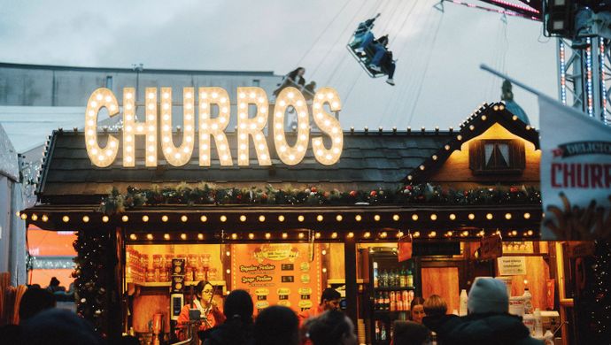 Festive churros stall with illuminated sign and visitors browsing at a Christmas market.