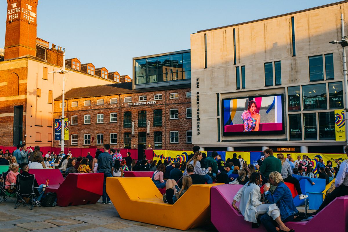 Audience gathered in Millennium Square watching a presenter on Leeds Big Screen during a live event