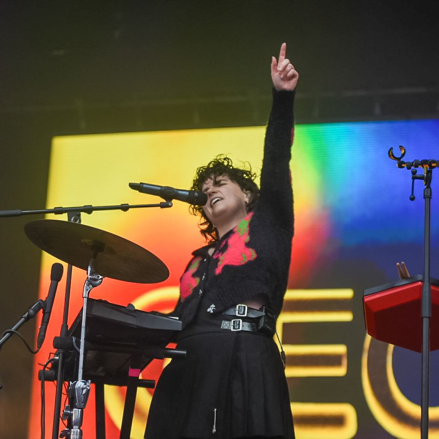 Georgia singing and playing drums on stage at Millennium Square, raising one arm in front of a colourful light display.