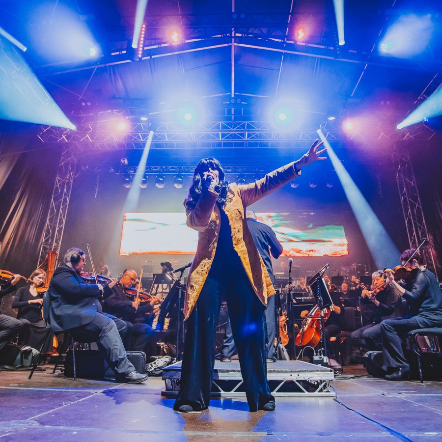 Singer performing on stage on the square with the orchestra and a large screen behind them.