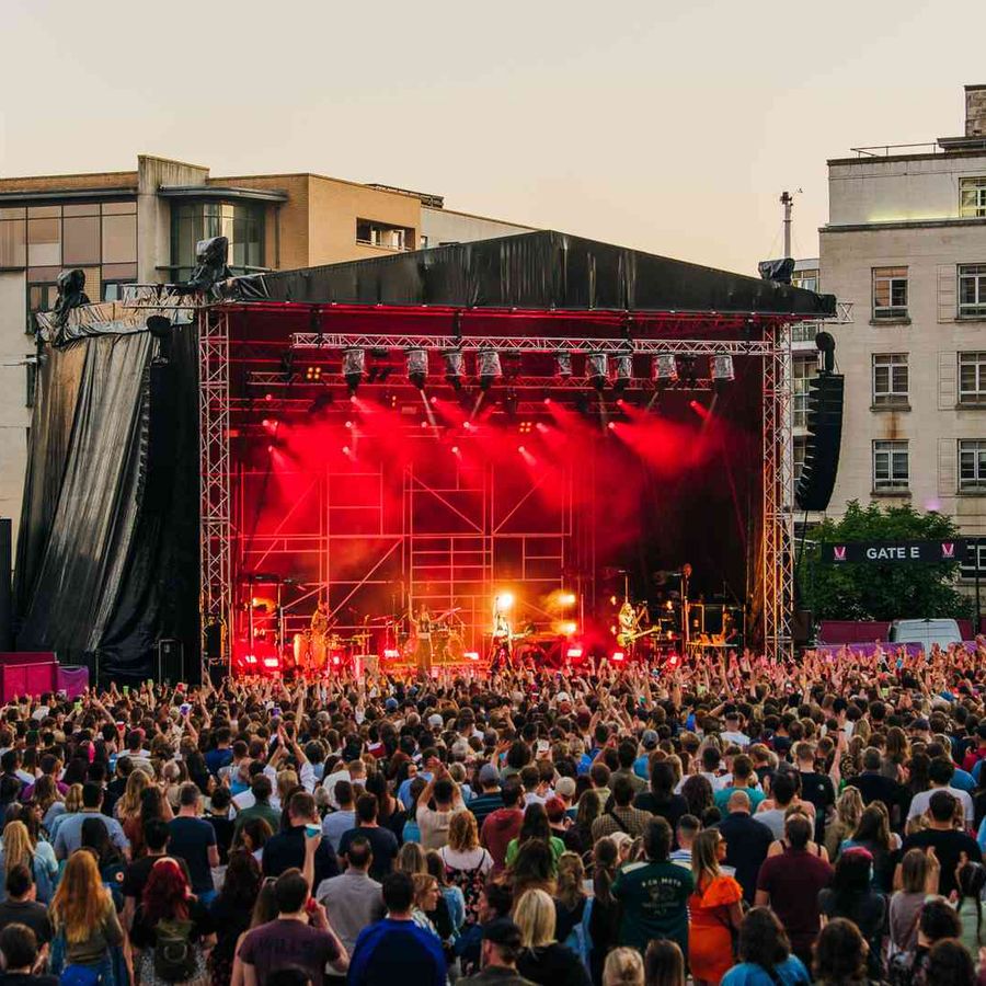 Large outdoor concert crowd watching stage with red lighting and band performing.