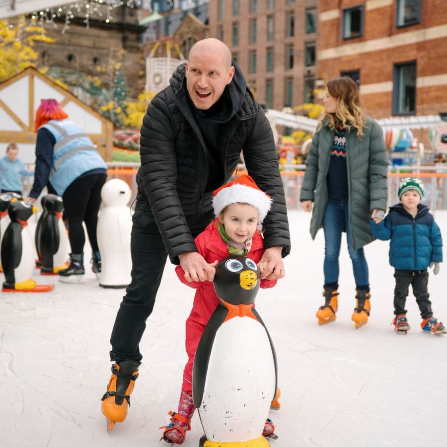Family-friendly ice skating session with a child using a penguin skating aid on an outdoor rink.