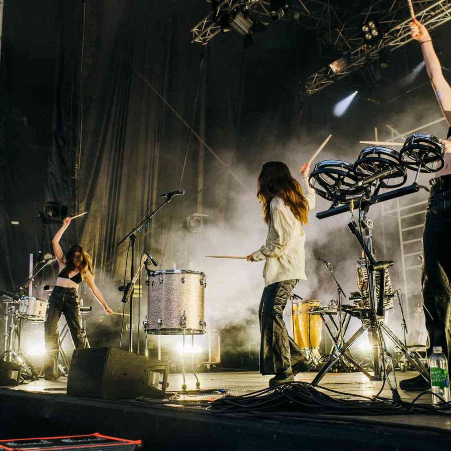 Haim playing drums and percussion instruments on stage with bright concert lighting.