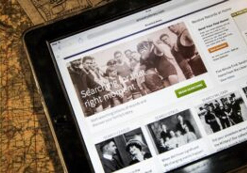 A tablet displaying a historical website with black-and-white photos and text, placed on a table with an old map beneath it.