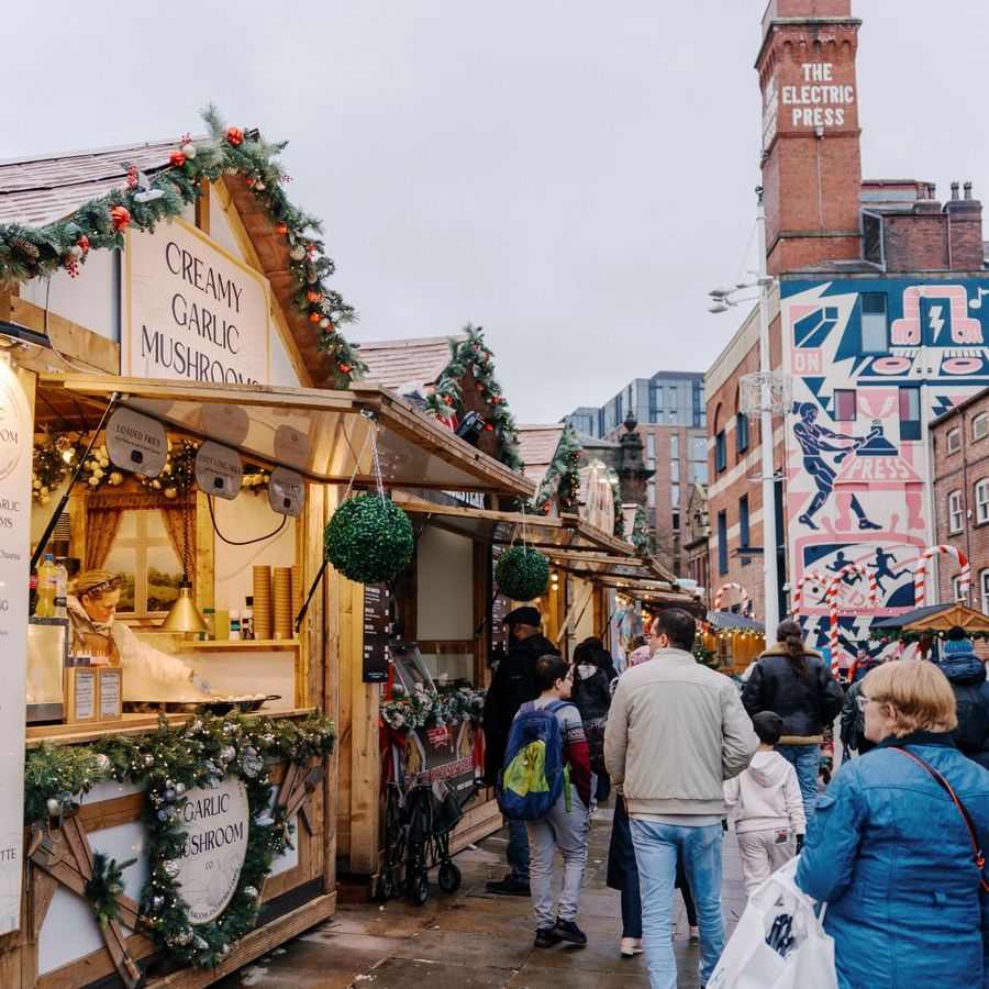 Festive Christmas market stalls and shoppers outside The Electric Press, decorated with seasonal garlands and lights.