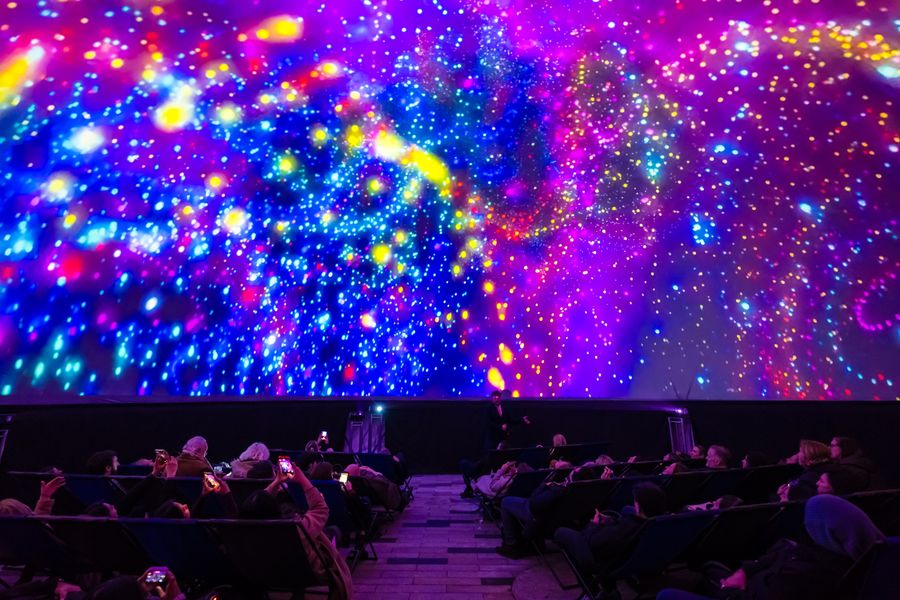 Visitors watch a colourful immersive galaxy projection on the dome screen of a planetarium.