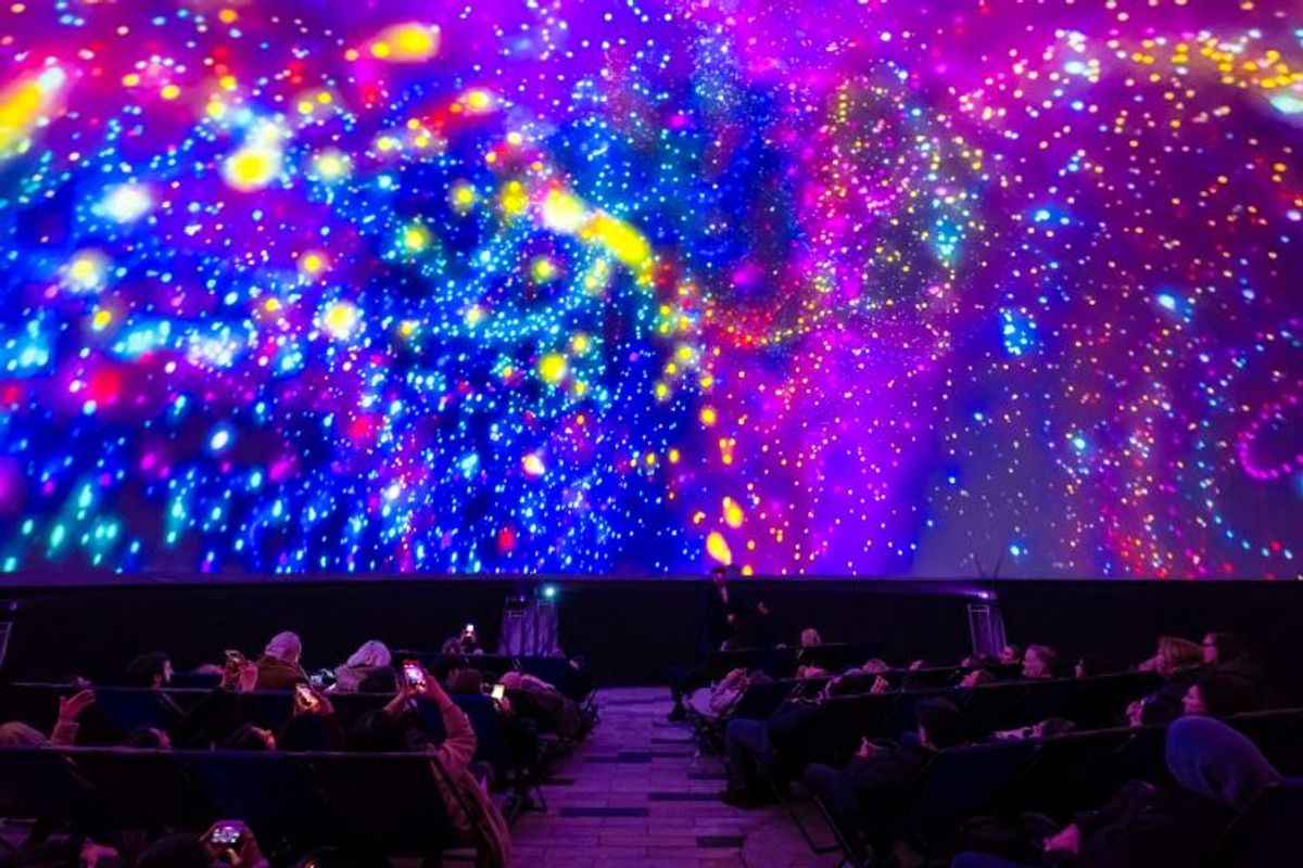Visitors watch a colourful 360° projection of stars and galaxies inside an immersive planetarium dome.