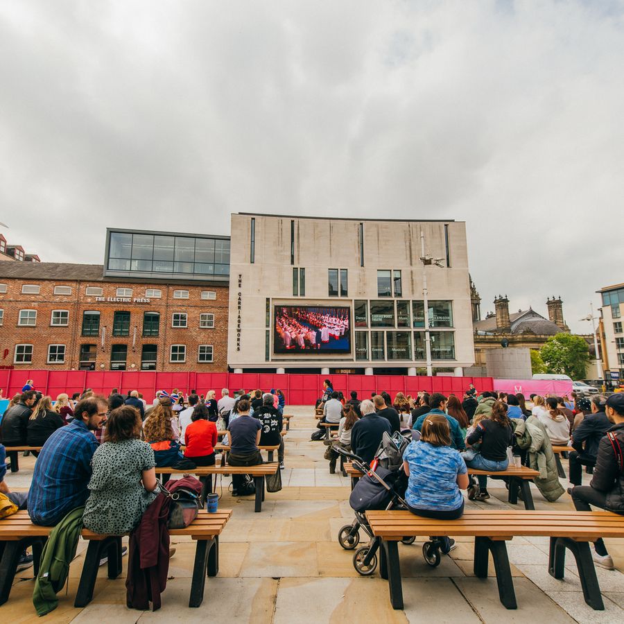 People sat on benches watching Leeds Big Screen