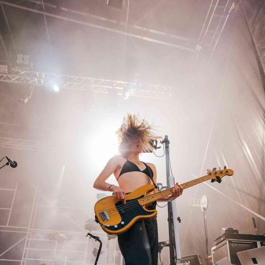 Musician playing bass guitar on stage surrounded by haze and lighting rigs.